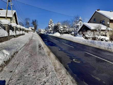 DW 941; widok drogi i chodnika przedstawiający ich zimowe utrzymanie; na zdjęciu widoczne drzewa, ogrodzenie, błękitne niebo
